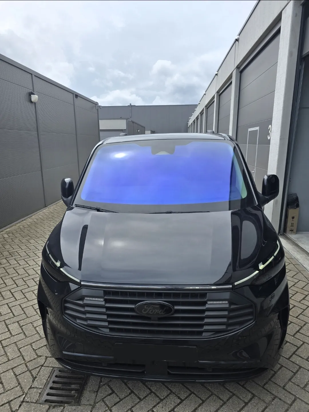 Zwarte bestelbus met blauw reflecterende chameleon folie op de voorruit