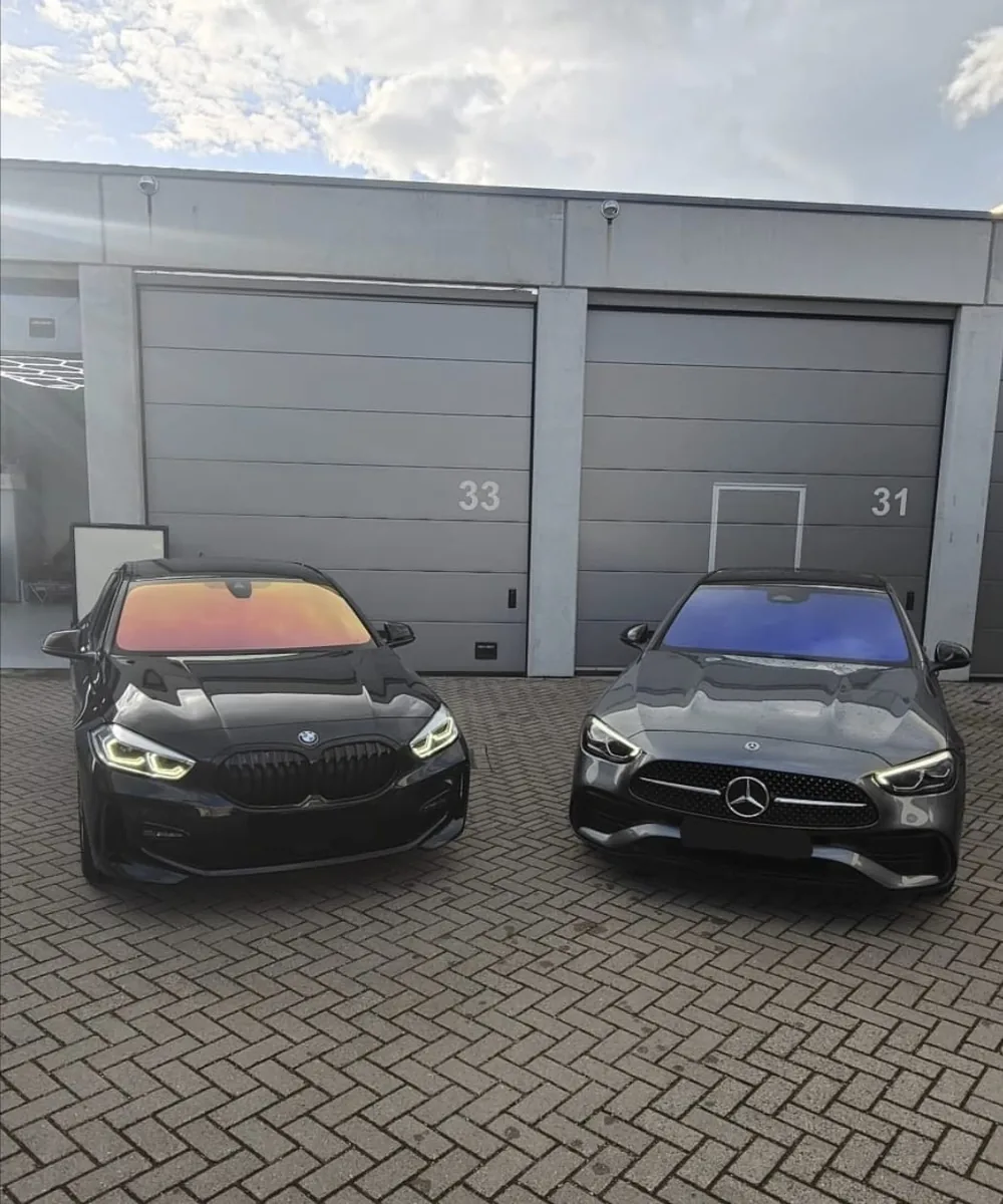 Zwarte BMW X2 en grijze Mercedes met getinte vooruiten, geparkeerd voor de werkplaatsboxen