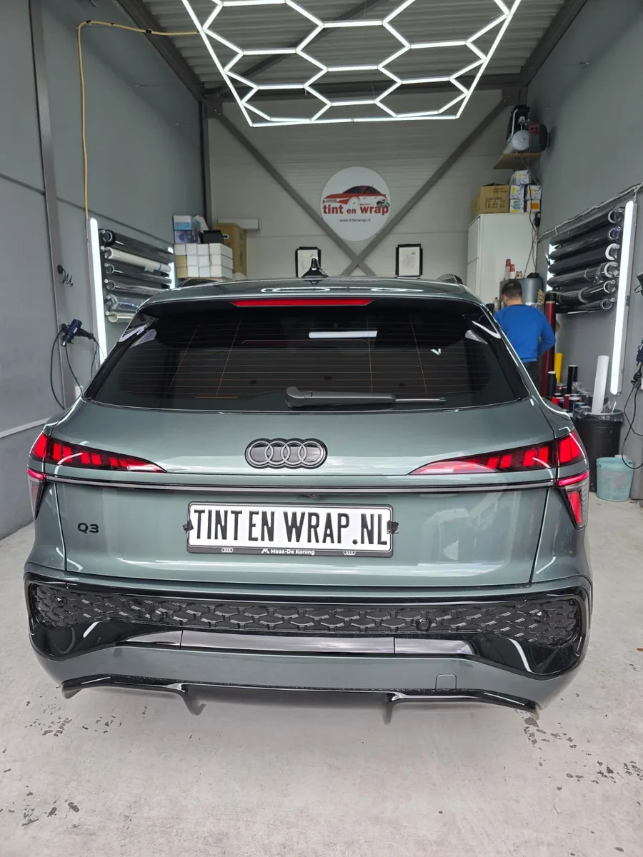 Grijze Audi Q4 e-tron met getinte achterruit en TINT EN WRAP.NL-bord in de werkplaats