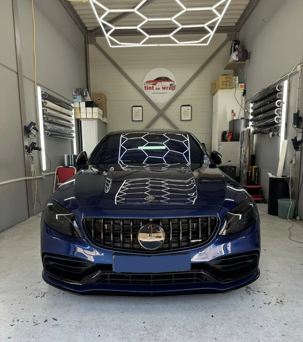 Donkerblauwe Mercedes C63 AMG met getinte voorruit, gefotografeerd van voren in de werkplaats
